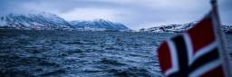 Fjell og hav i vintermørket, med norsk flagg i forgrunnen