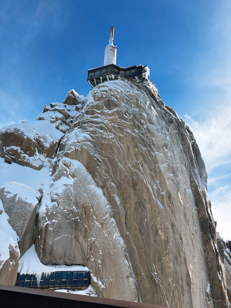 En fjelltopp sees nedenfra og opp, turisthytte på toppen.